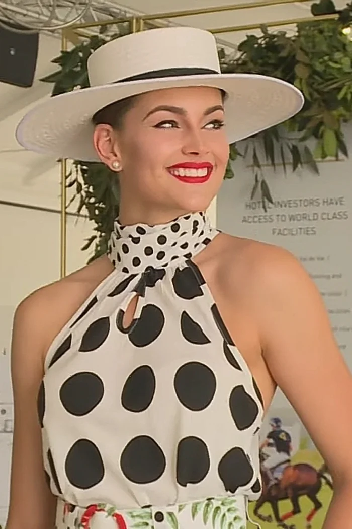 Rolene Strauss en robe à pois, chapeau blanc et rouge à lèvres vif lors d'un événement de polo