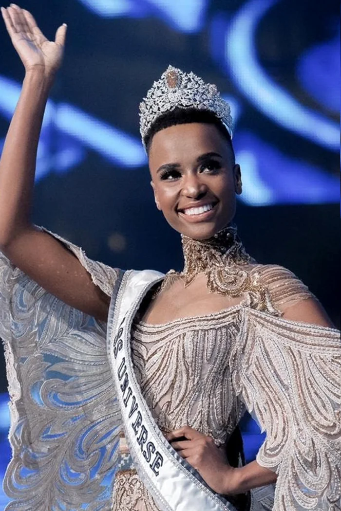 Zozibini Tunzi souriante avec couronne de Miss Univers et robe de scène argentée