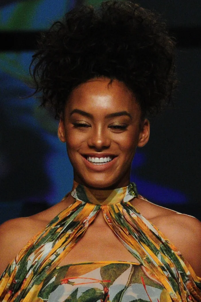 Raissa Santana souriante sur un podium, afro relevé et robe tropicale orange et verte