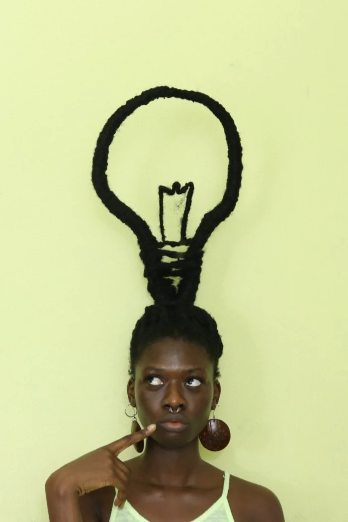 Laetitia Ky avec sculpture capillaire en forme d'ampoule sur fond vert clair