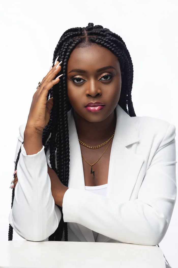 Morijah en portrait studio avec longues tresses, blazer blanc et maquillage rose