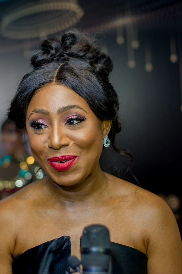 Dakore Akande en portrait d'evenement avec chignon noir, maquillage violet et rouge a levres rouge