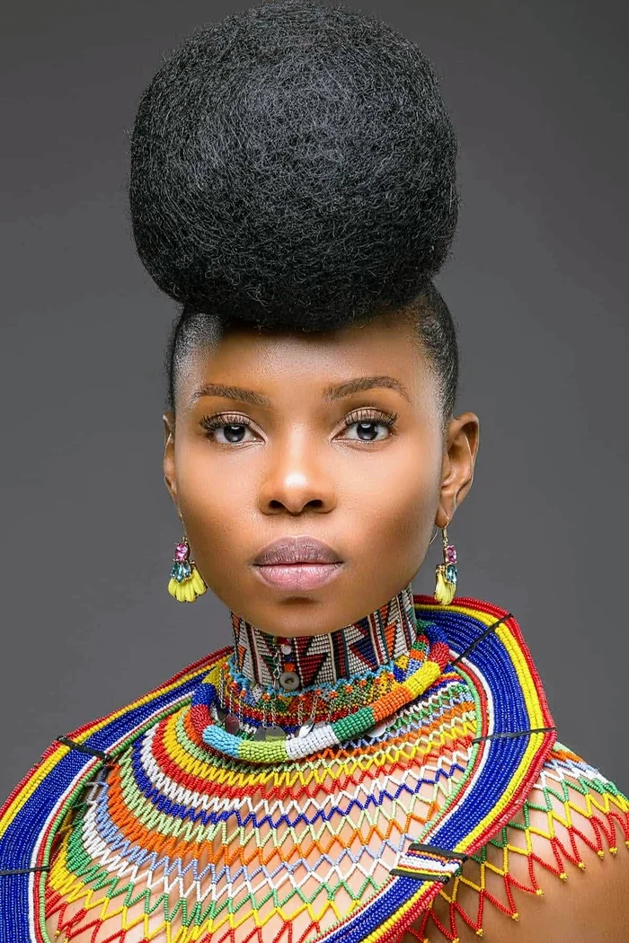 Yemi Alade en portrait studio avec coiffure haute noire, bijoux colores et tenue perlee multicolore
