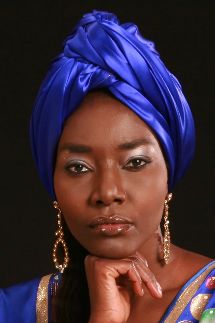 Coumba Gawlo Seck en turban bleu intense, bijoux dorés et regard frontal