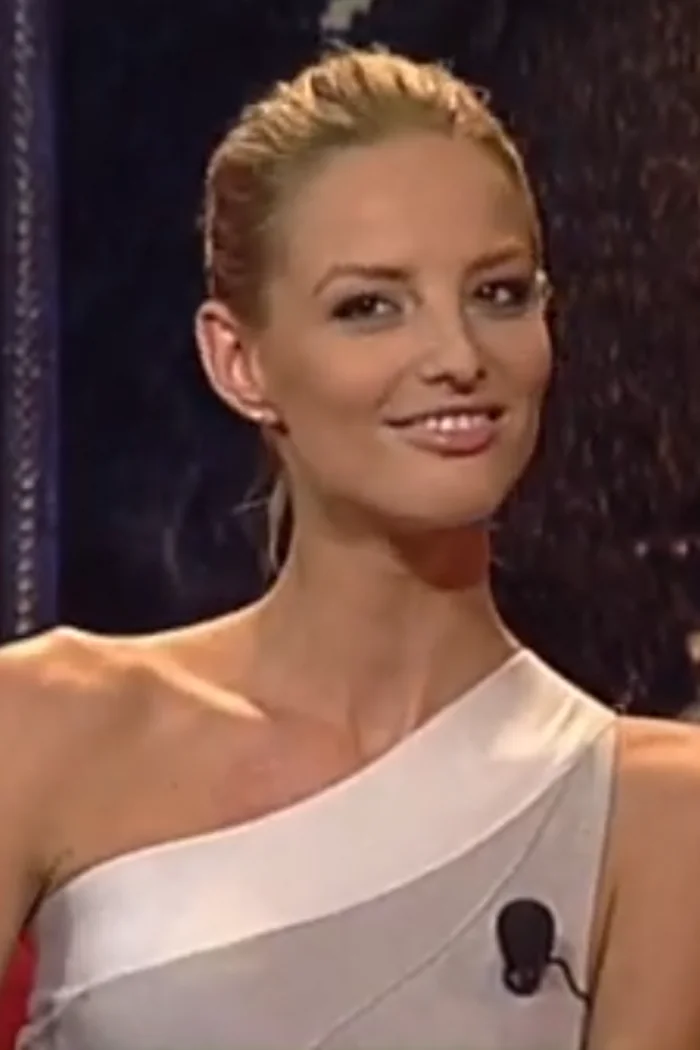 Michaela Kocianova en robe claire asymetrique, cheveux blonds releves et fond sombre de plateau