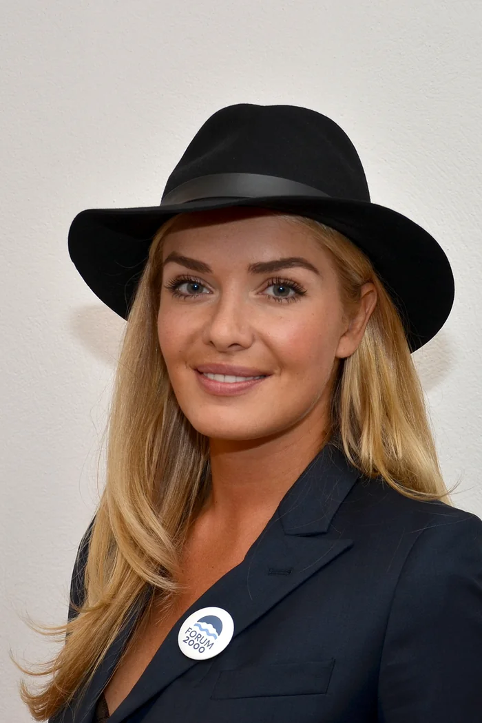 Tatana Kucharova en blazer noir et chapeau noir, portrait lumineux sur fond clair