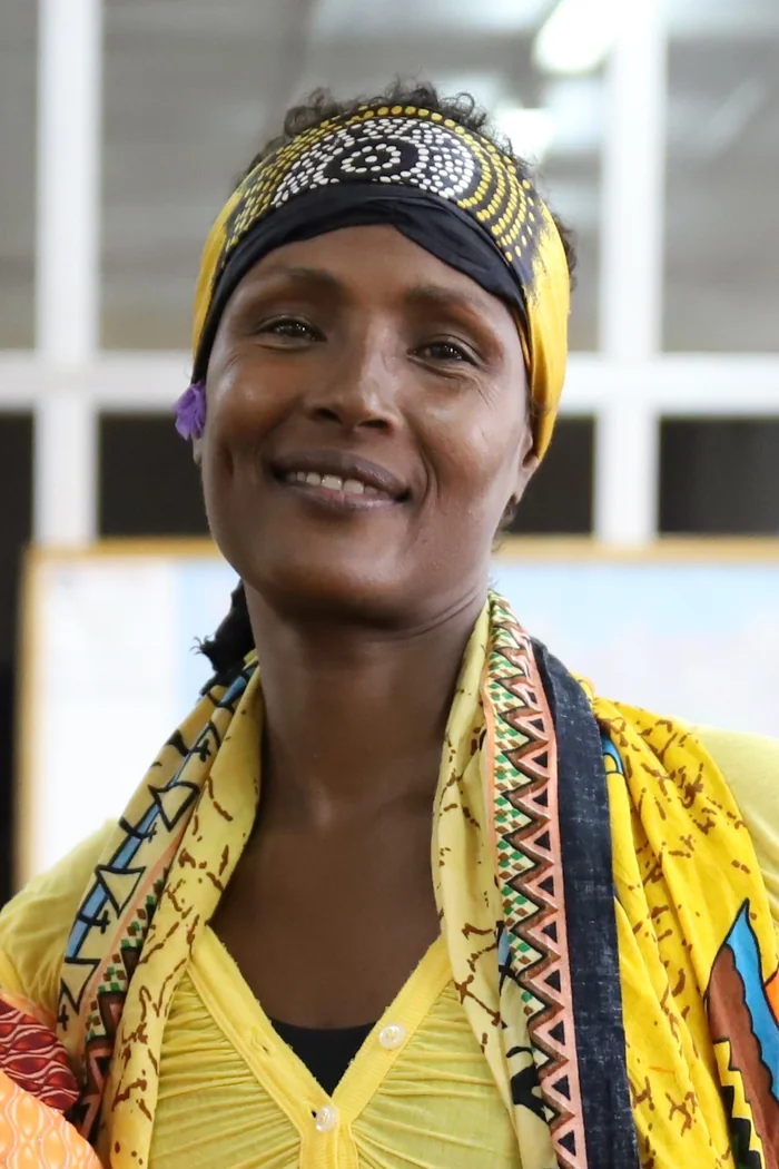 Waris Dirie souriante avec foulard imprime jaune et noir et vetement traditionnel colore