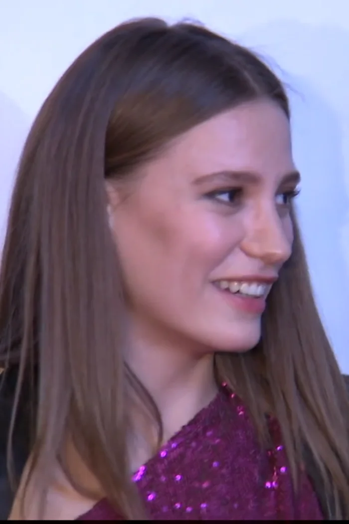 Serenay Sarıkaya de trois-quarts, cheveux châtain clair, tenue à sequins violets sur fond bleu.